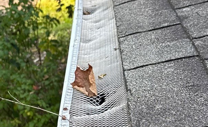 Hail-bruised shingles and dented gutter on a Buda home